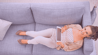 Woman laying on couch while holding tablet