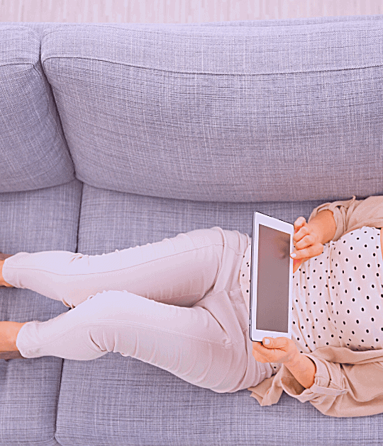 Woman laying on couch while holding tablet