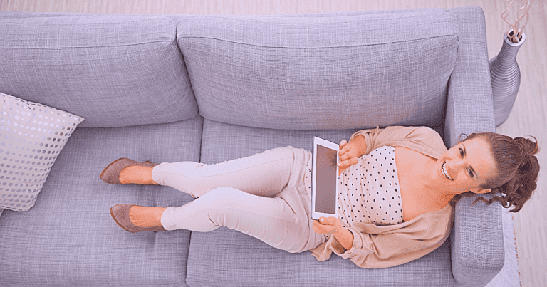 Woman laying on couch while holding tablet