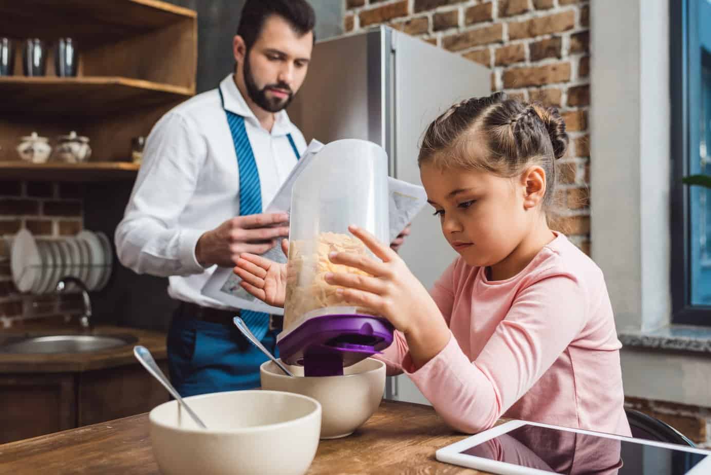 girl pouring cereal and father reading paper